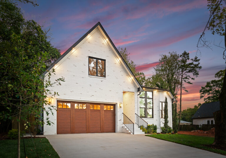 White brick exterior at twilight with a lit garage and driveway